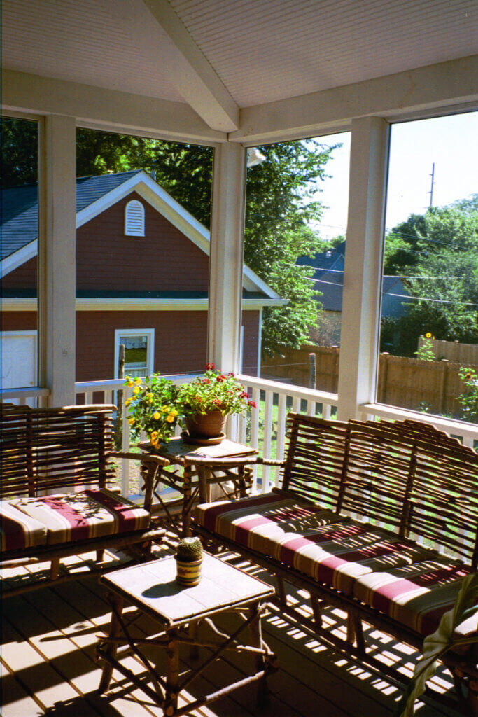 Screened-in porch with rustic wicker furniture, striped cushions, and potted plants overlooking the backyard.